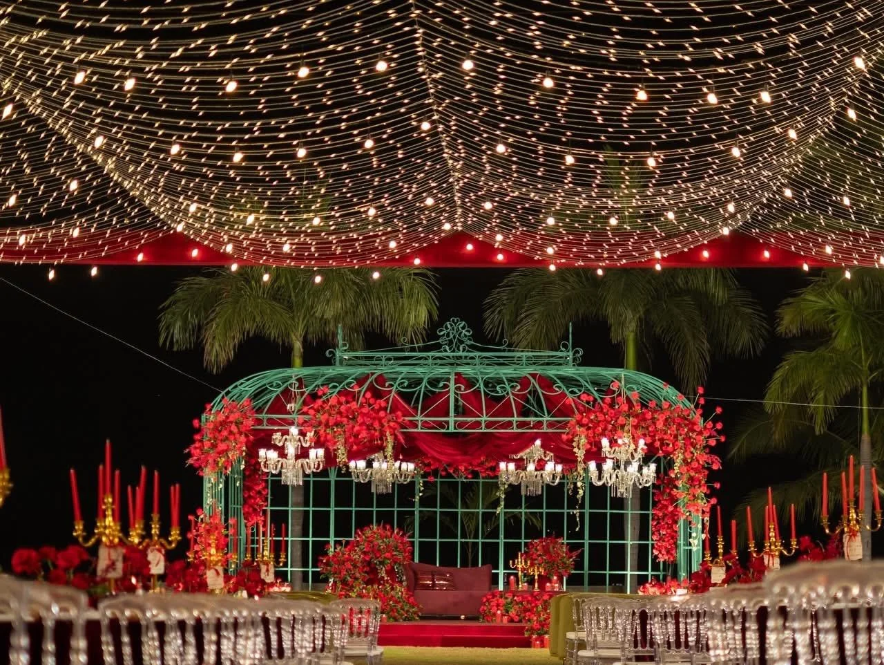 Rich red wedding celebration setting with glowing overhead string lights and floral centerpieces